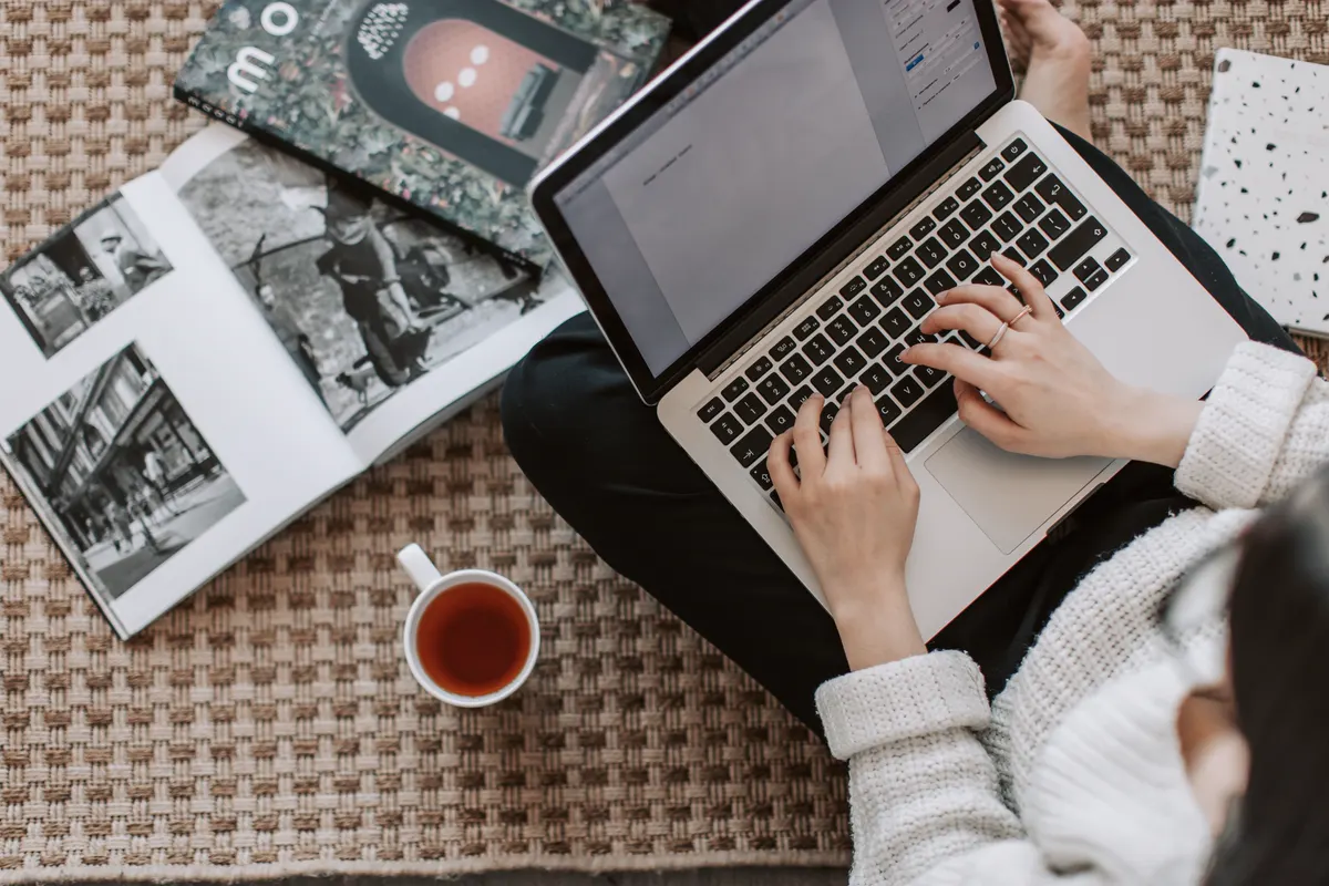 Persona trabajando con una computadora y material de referencia para crear contenido